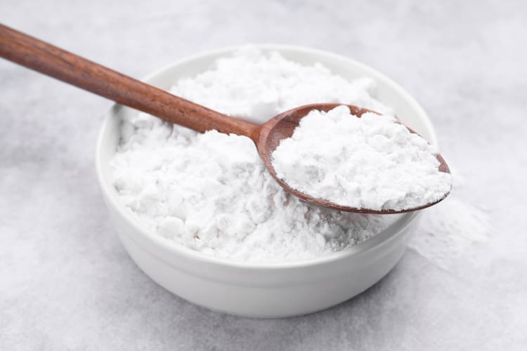 A spoonful of flour on top of a heap of it in a bowl
