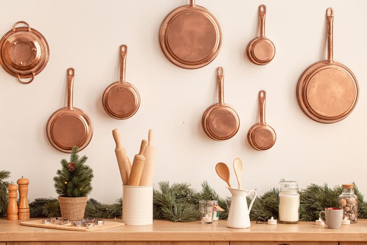 A kitchen setting with copper pots and pans hanging on a wall above other utensils