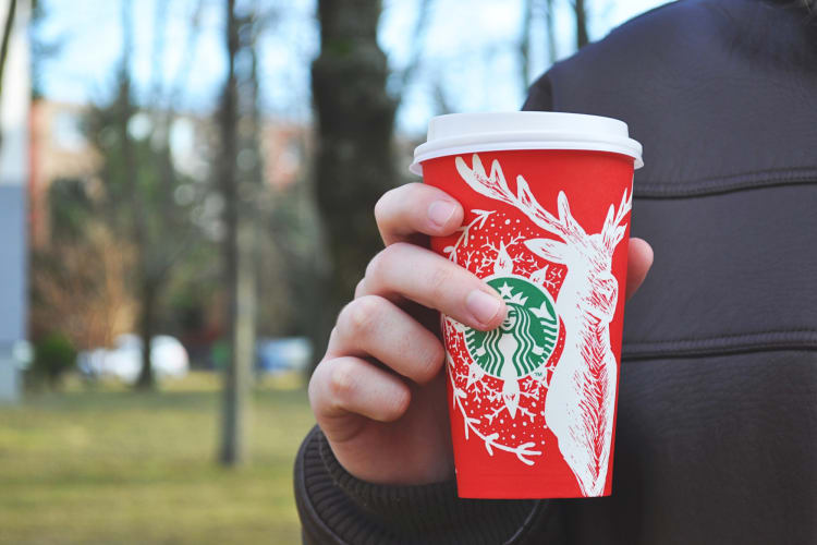 A hand holding a festive season-themed takeaway Starbucks cup