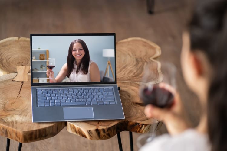 Two people drinking wine, one on a laptop and one in person