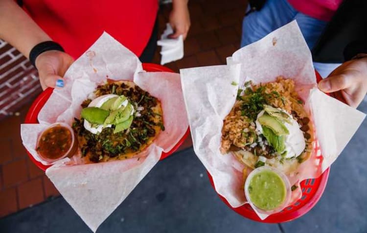 Two people's hands holding baskets of food from food trucks