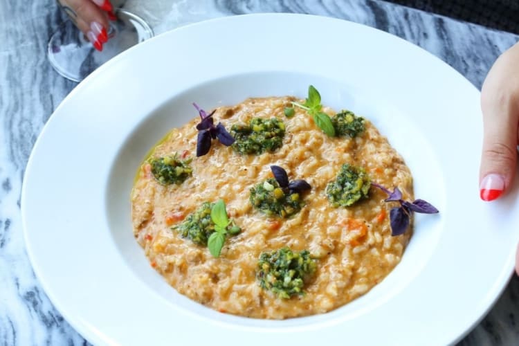 A bowl of risotto topped with pesto and edible flowers