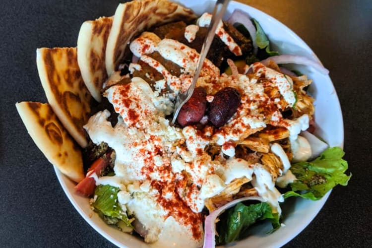 A bowl with hummus, pita, salad and olives