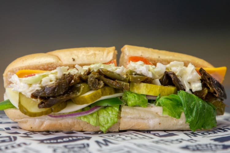 A sub sandwich filled with cheese, pickle, onions and salad