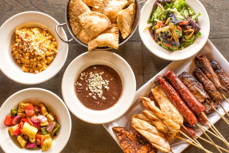 Aerial view of meat skewers, corn, empanadas, salad, vegetables and refried bean dip