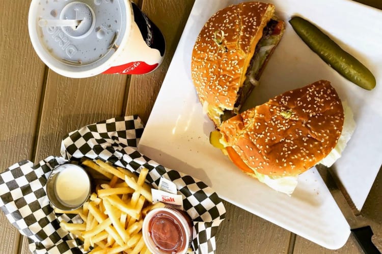 Burger cut in half served with a dill pickle, fries and a coke