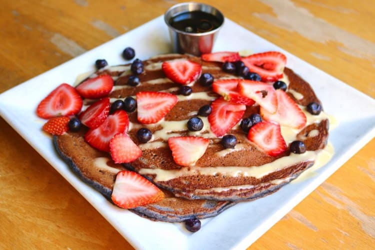 Pancakes toppes with blueberries, strawberries and drizzle with sweet sauce