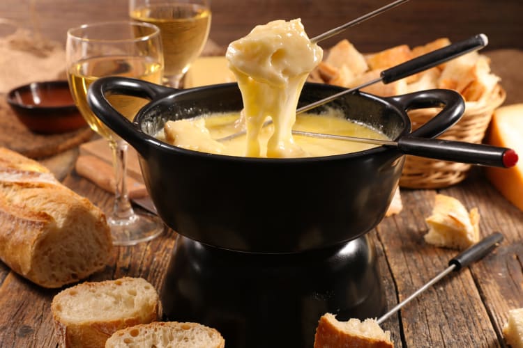 A piece of food held up by a skewer coming out of a cheese fondue