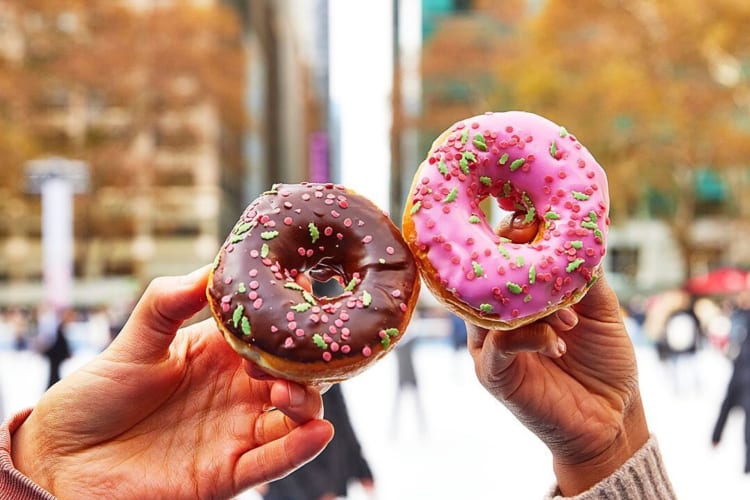 Two hands holding two doughnuts from Dunkin' Donuts