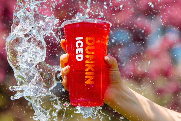 A splash of water surrounding a hand holding a Dunkin' Donuts drink