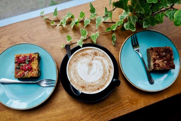 A cappuccino next to two slices of cake on blue plates