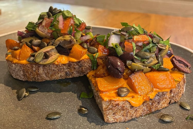 Roasted butternut squash on toast topped with olives, pumpkin seeds and salad