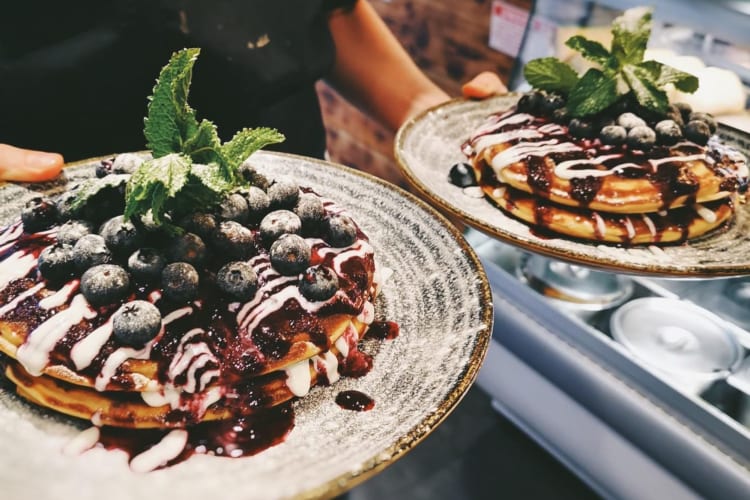 Two American-style pancakes topped with blueberries and icing sugar being served for breakfast in Edinburgh.