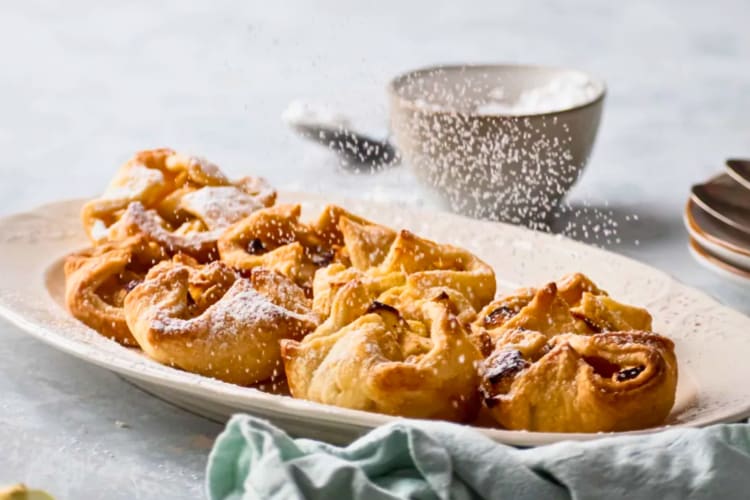 Mini apple pies being dusted with icing sugar.