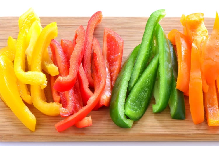 Sliced yellow, orange, red and green bell peppers on a chopping board.