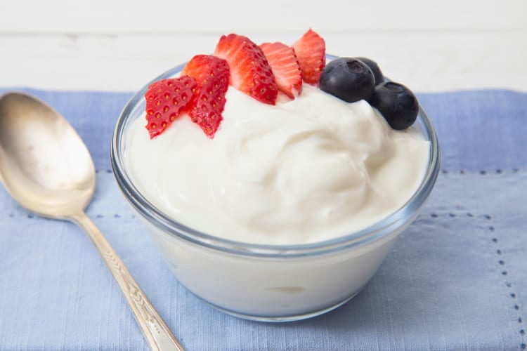 A bowl of yogurt topped with sliced strawberries and blueberries.