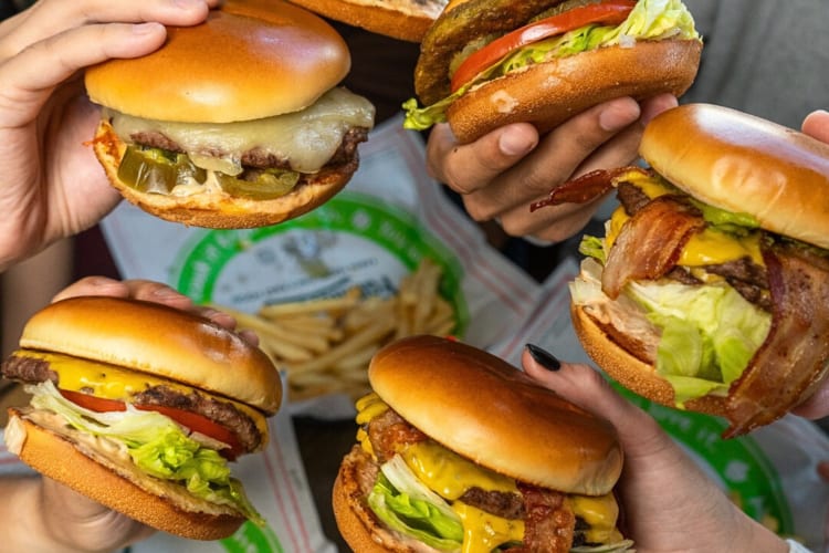 Five hands holding five burgers from Farmer Boys