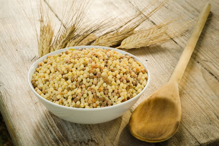 Fregola on a plate and a wooden spoon