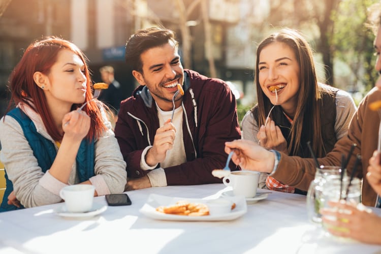 Three people laughing while enjoying a meal at an outdoor table of a restaurant