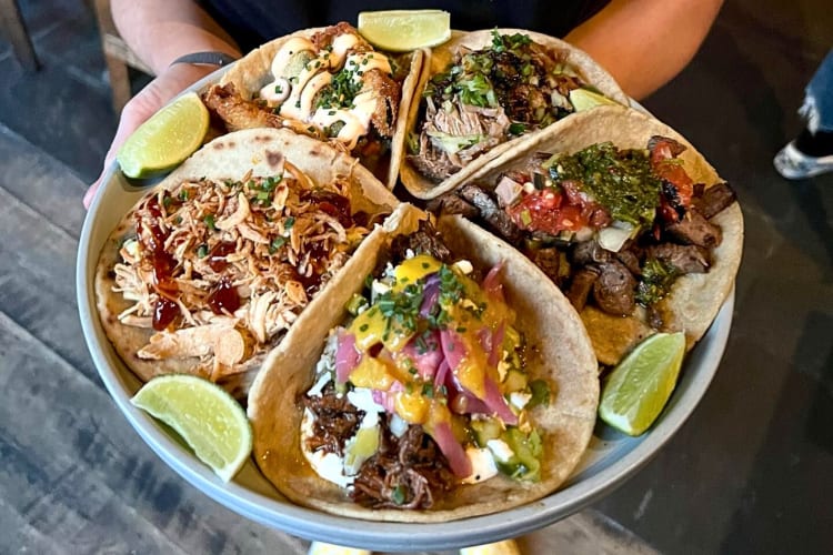 Hands holding a plate with five tacos from Loco Taqueria & Oyster Bar 