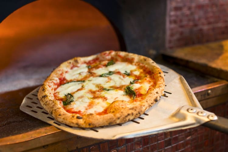 A pizza coming out a wood-fired oven.