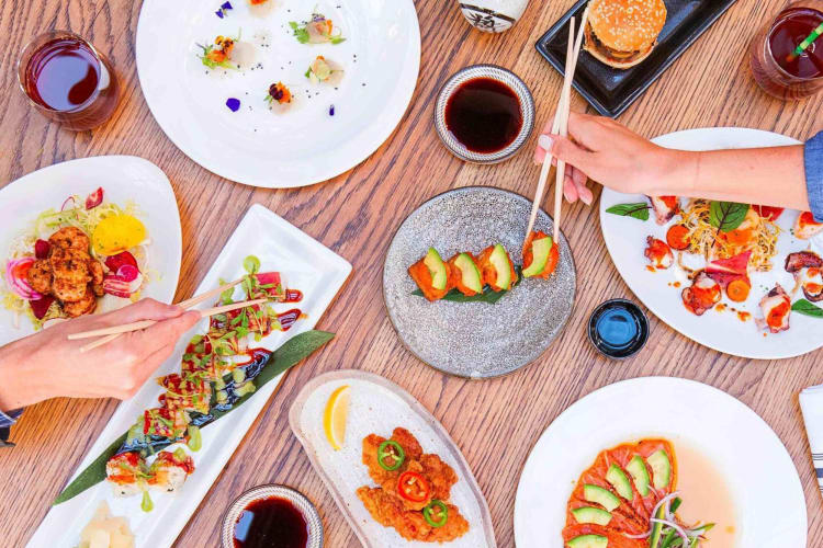 Two hands eating from various meals at Sushi Roku in Las Vegas