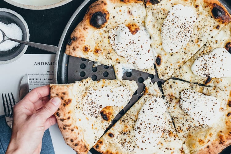 A hand grabbing a slice of cacio e pepe pizza