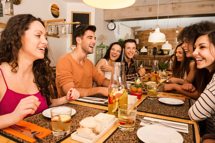 Seven friends chatting and laughing while dining at a restaurant