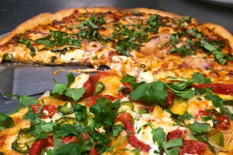 This customized pie has half basil and red onion and half goat cheese, jalapeño, red bell pepper, crispy potatoes, capers and cilantro.