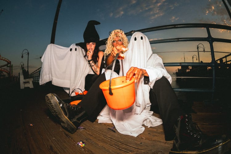 three people sit on a bench outdoors in halloween costumes