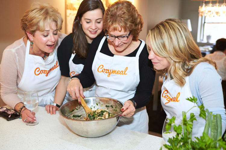 Four women looking at a bowl of food being stirred during a cooking class