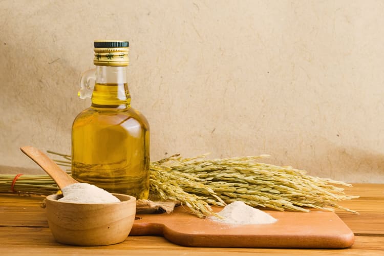 A bottle of rice bran oil surrounded by rice bran and rice grain
