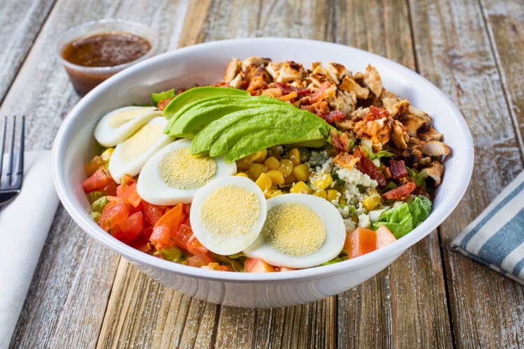 A bowl of Cobb salad on a wooden table.