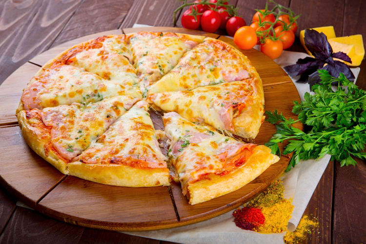 A pizza on a wooden board, surrounded by tomatoes, spices and herbs
