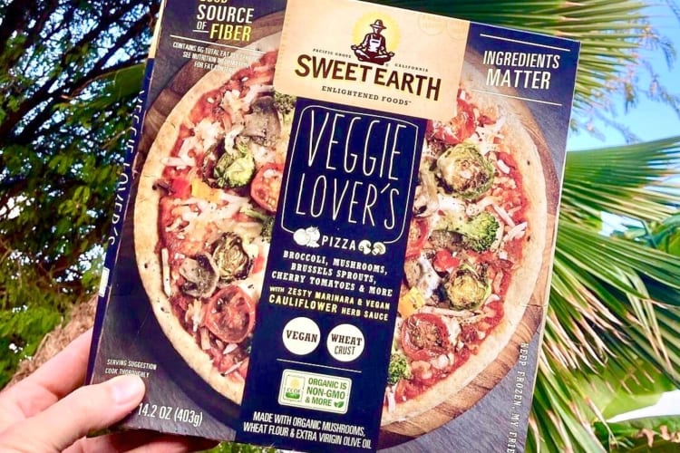 A hand holding a Sweet Earth Veggie Lover’s Pizza box, one of the healthiest frozen pizzas