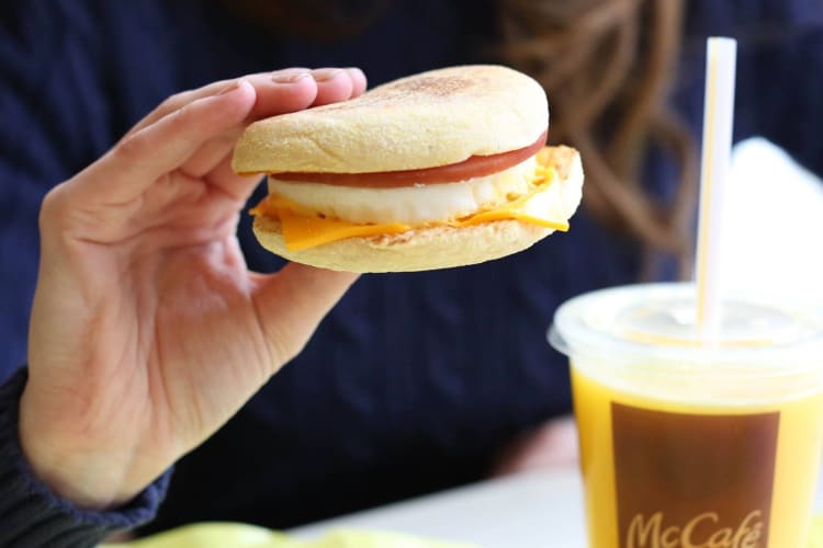 Hand holding up an Egg McMuffin next to a cup of orange juice.