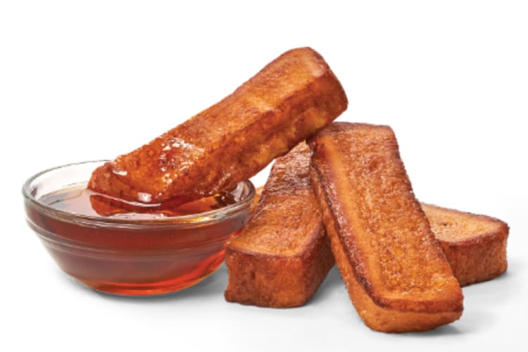 Four warm, fluffy French toast sticks with syrup on the side.