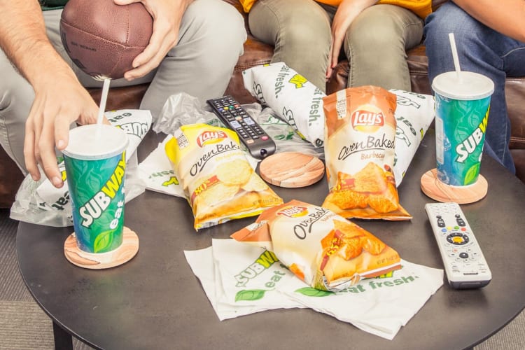 Subway drinks and food on a table with people on the couch behind.