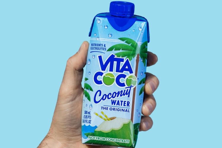 A hand holding up Vita Coco coconut water.