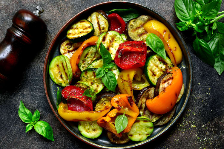 A plate of cooked vegetables next to a salt shaker