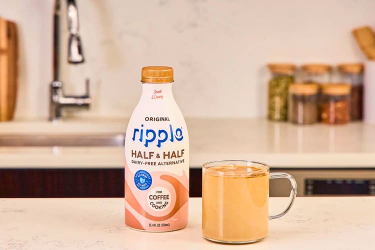 A bottle of creamer next to a cup of coffee.