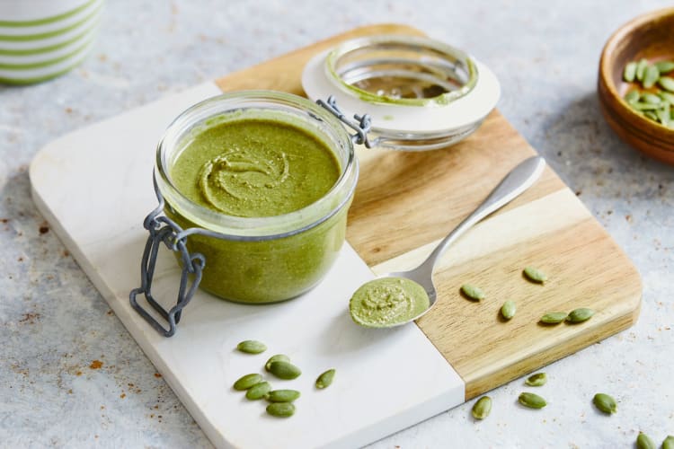 A jar of pumpkin seed butter next to seeds.