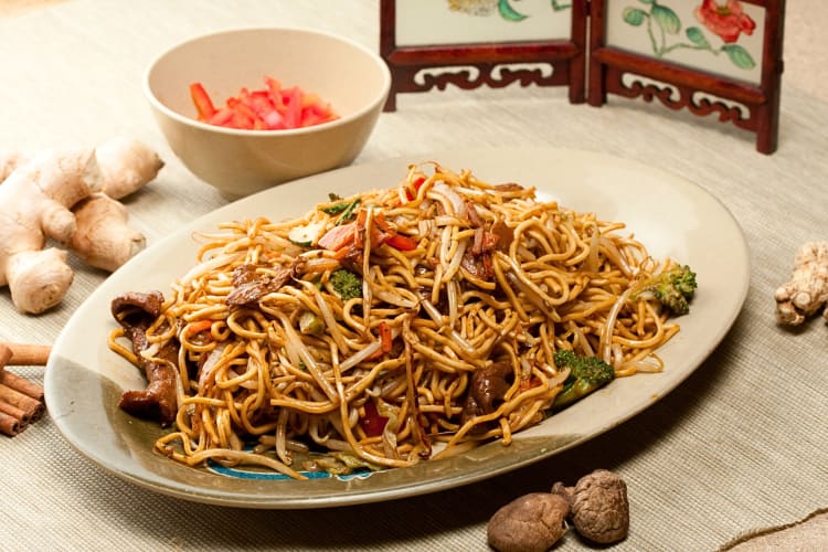 A large serving plate of fried beef noodles surrounded by raw ingredients
