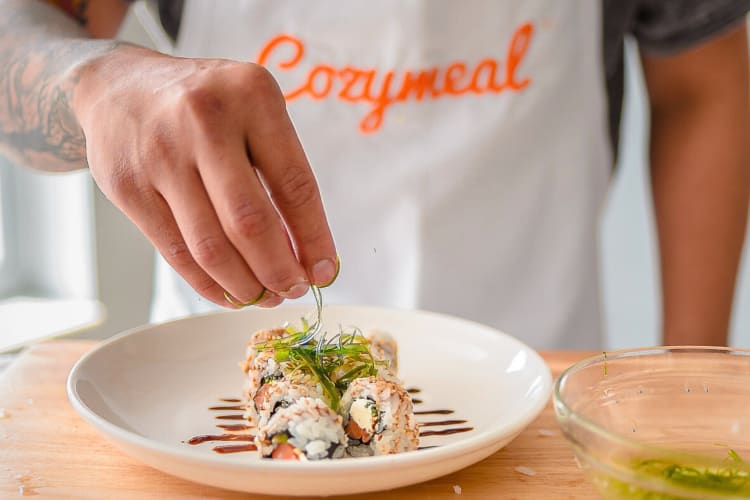 Close-up of a person's hand garnishing sushi during a cooking class booked on Cozymeal