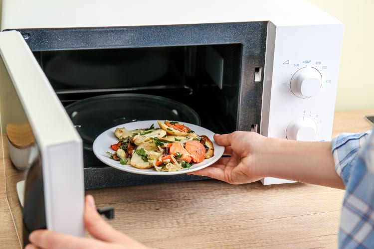 Woman Putting Plate with Food in Microwave Oven.