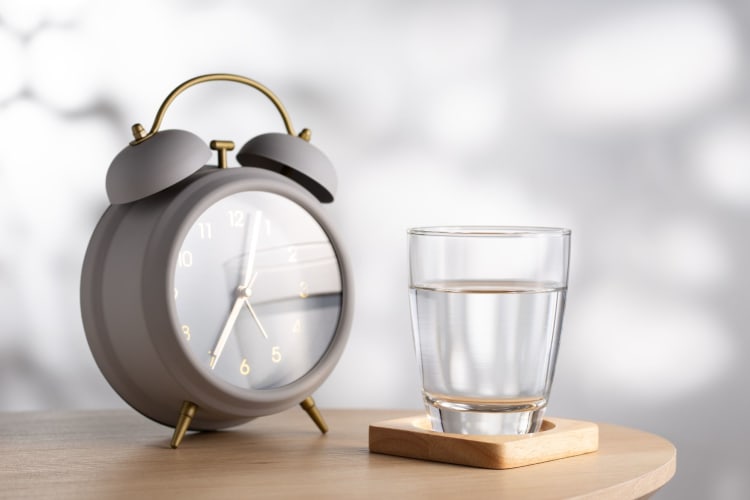A glass of water next to an alarm clock on a bedside table.