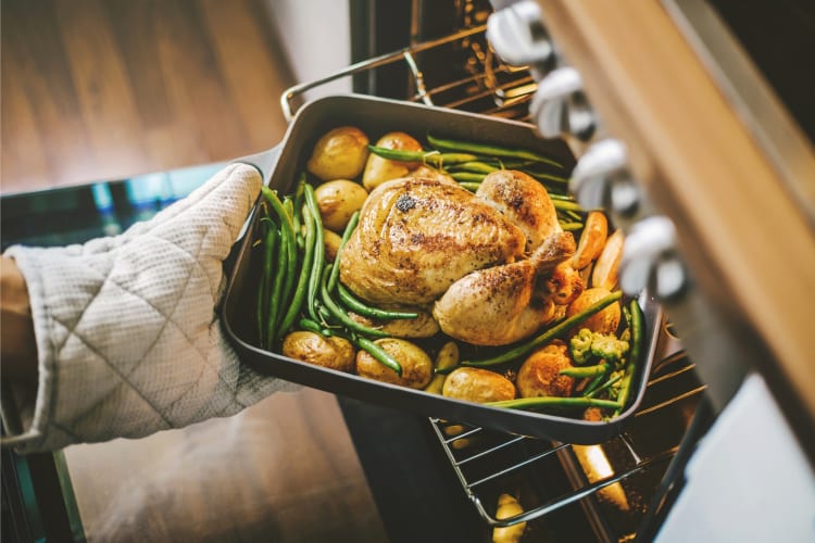 A chicken with vegetables and potatoes being taken out of the oven