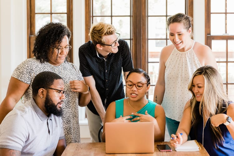 A team of six discussing something in front of a laptop