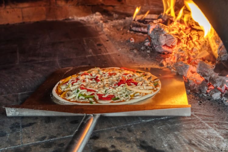 Pizzeria putting pizza in a wood-fired oven.