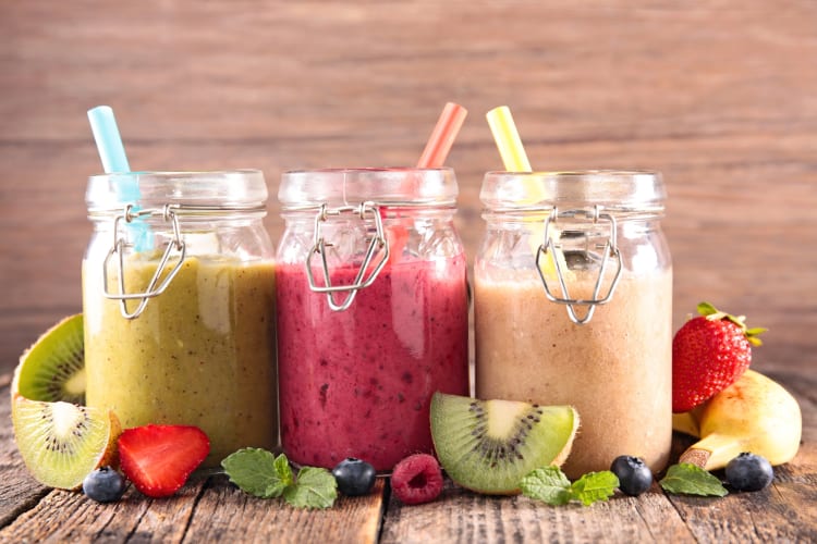 Three smoothies in glass jars surrounded by fruit